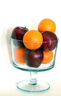A glass pedestal bowl filled with apples and oranges.