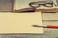 An old poetry book, glasses, paper and a calligraphy pen on a table.