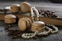 An elegant still life of coffeebeans, almond cakes and a string of pearls on wood.