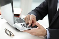 Man using a calculator next to a laptop.