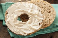 Fresh cream cheese spread over a whole wheat bagel on a cloth napkin.