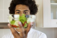 Young man holding up bowl of salad.