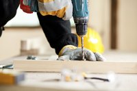A close-up of a carpenter drilling a hole with a drill bit.
