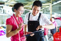 A manager and designer at a clothing factory look at documents on a clipboard