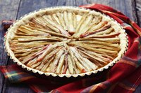 Roasted rhubarb arranged in a pie crust on a rustic table with a plaid cloth napkin.