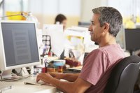 A man types on his desktop computer in an office setting.