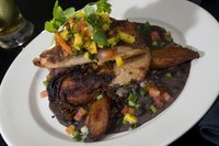 Traditional jerk chicken on a plate served with black beans and rice, plantains, cilantro and fresh mango salsa.