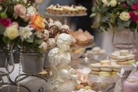 An assortment of decadent desserts on a table with flower arrangements and a romantic sculpture.