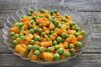 A glass dish of peas and carrots on a rustic table.
