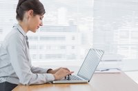 A businesswoman sits at her desk, typing on a laptop computer