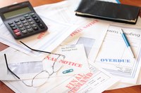 Stack of overdue bills on table with calculator and eye glasses.