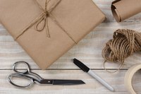 A gift wrapped in brown butcher paper sitting on a table with scissors, tape, string and a marker.