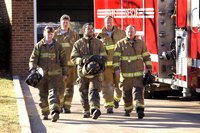 A pack of firemen walking out of a station.