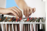 Woman's hands flipping through a filing cabinet.