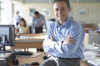 A mature businessman holding his arms across his chest while smiling.