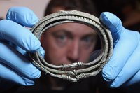 An archaeologist examining a metal arm ring from 900 A.D.