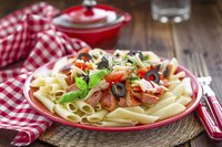 A plate of pasta topped with chicken, tomatoes, olives, cheese and basil.