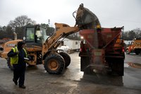 A front end loader dumping salt and sand into the back of a dump truck.