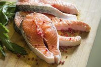 Fresh salmon steaks on a cutting board with red peppercorns and parsley.