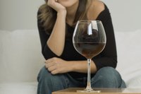 A glass of red wine in front of a woman sitting on a sofa.