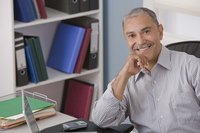 A smiling man is sitting in front of his laptop at his desk.