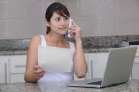 A woman is working on her laptop and talking on the phone.