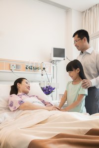 Father and daughter visiting mother in hospital bed.