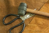 A black rubber mallet lying next to a pair of scissors on a piece of leather.