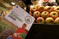 A pamphlet promoting quality produce near an apple bin in a market.