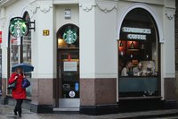 A pedestrian with an umbrella walking past a Starbucks franchise.