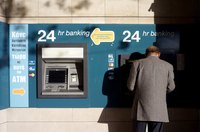 A bank customer utilizing automated banking at an ATM machine on the sidewalk.