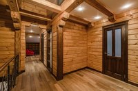 Wood beams across a cabin celing that is painted white with light fixtures.