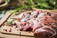 Venison meat on a cutting board with herbs and spices.