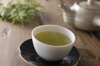A teapot and cup of hot green tea on a table.