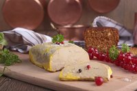 A slice of foie gras on a cutting board with garnish.