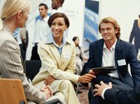 A group of young adults with name tags and business packets sit together at a trade show to discuss their respective businesses