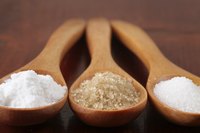 A scoop of turbinado sugar in between spoonfuls of powdered and white granulated sugar.