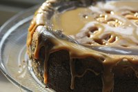 A decadent cheesecake dripping in homemade caramel on a glass pastry stand.