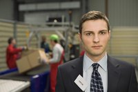 A businessman wearing a visitor's badge in a production facility.