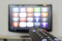 A close-up of a television remote facing a television screen.