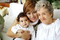 A woman sitting on the sofa with her young child and senior mother.