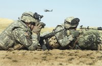 U.S. military soldiers using a gun and binoculars in the field.