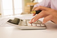 A close-up of a woman using a calculator and pen at her desk.