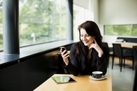 A woman using her smart phone and tablet in a cafe.