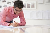 A man in casual business attire is writing a paper.