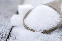 A wooden spoon filled with white sugar spills onto a table in front of sugar cubes.