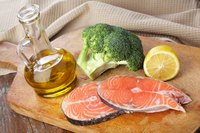 Two salmon filets on a cuttingboard wtih broccoli, lemon and oil.