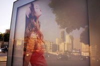 An advertisement reflecting in a bus stop window in the city.