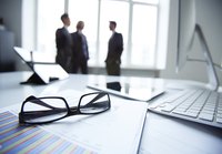 Close-up of business desk with three businessmen speaking in background