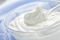 A glass bowl and spoon filled with sour cream.